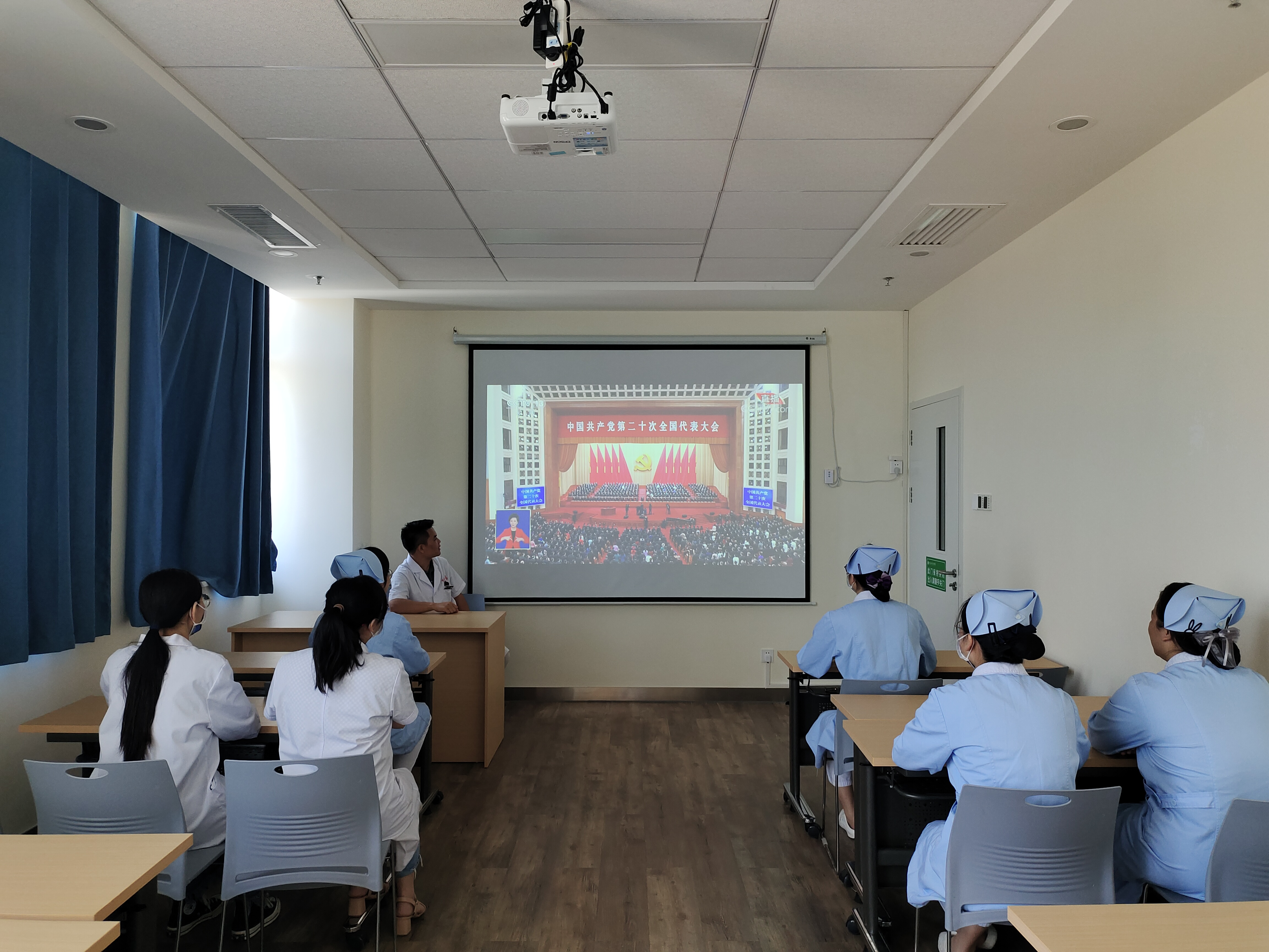 在百东院区肾内科，肾内科宣传委员邓高与其他党员同志和群众一起围坐在科室小教室的大屏幕前收看大会直播。